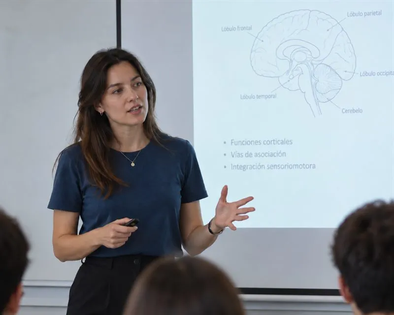 Docente explicando neuroanatomía a sus estudiantes frente a una proyección del cerebro